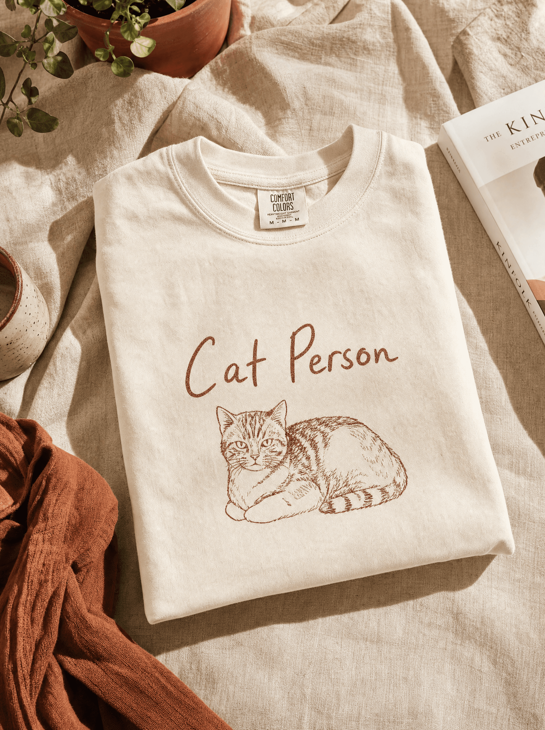 Heavyweight cream tee folded on cream linen with hand-drawn 'Cat Person' typography and illustrated cat