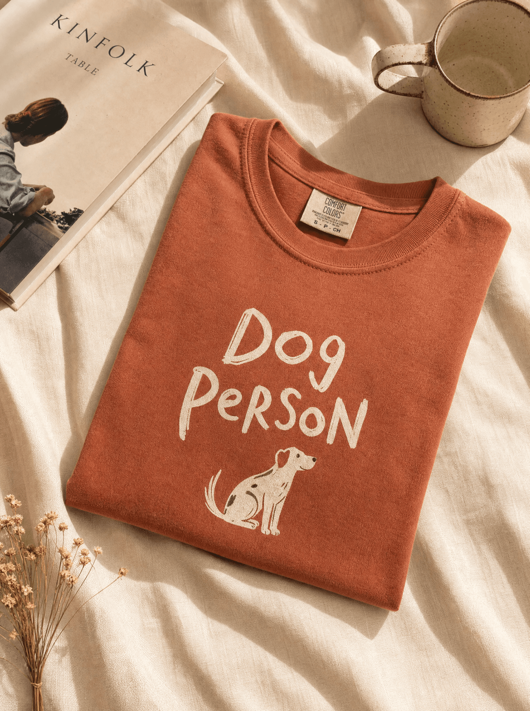 Heavyweight terracotta tee folded on cream linen with hand-drawn 'Dog Person' typography